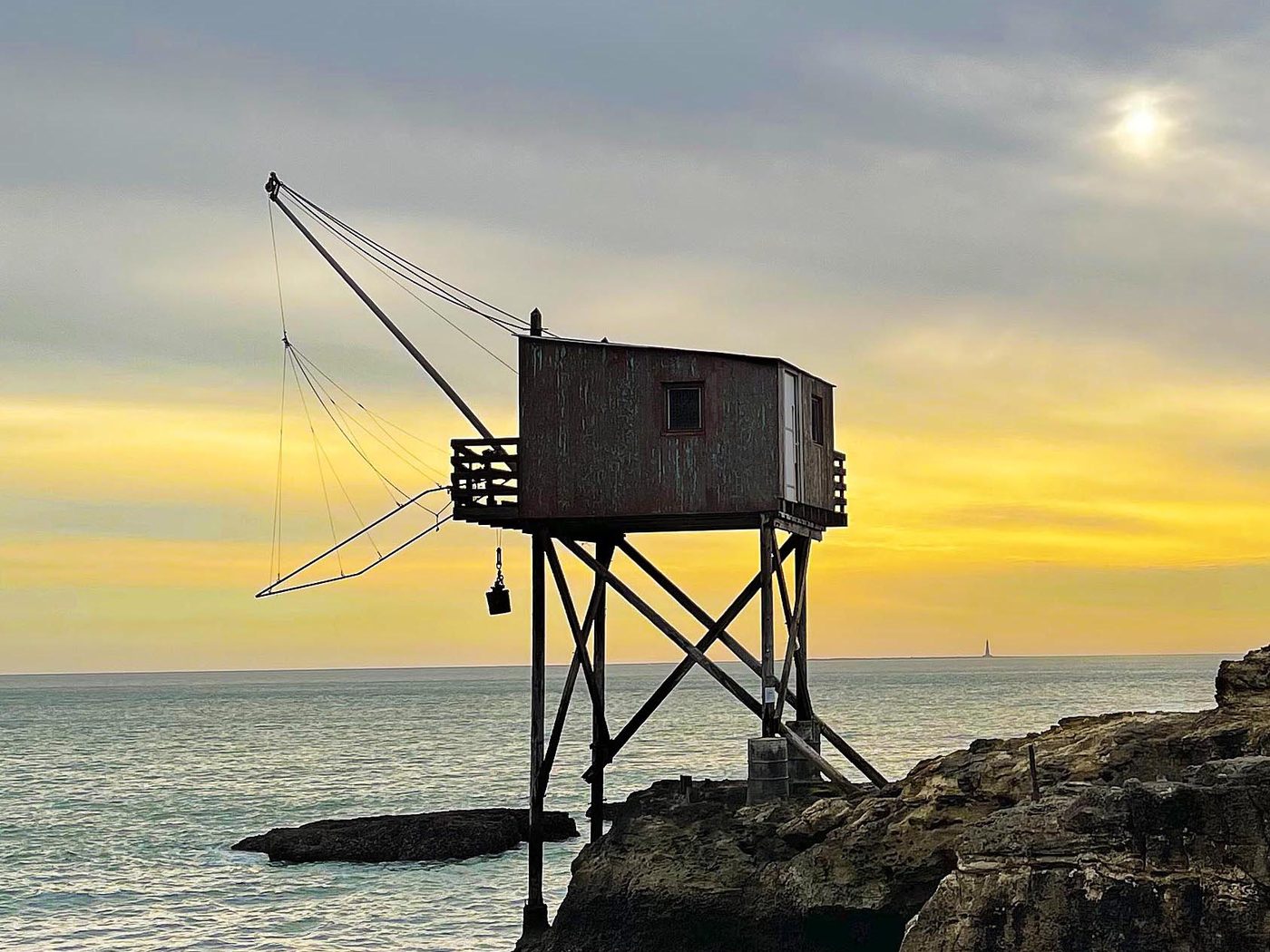 Carrelet de pêche en bois sur pilotis au coucher du soleil, filet et balancier au-dessus de l'océan Atlantique