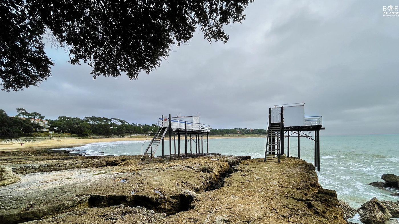 Deux carrelets blancs sur pilotis face à un ciel de tempête, plage rocheuse de Charente-Maritime