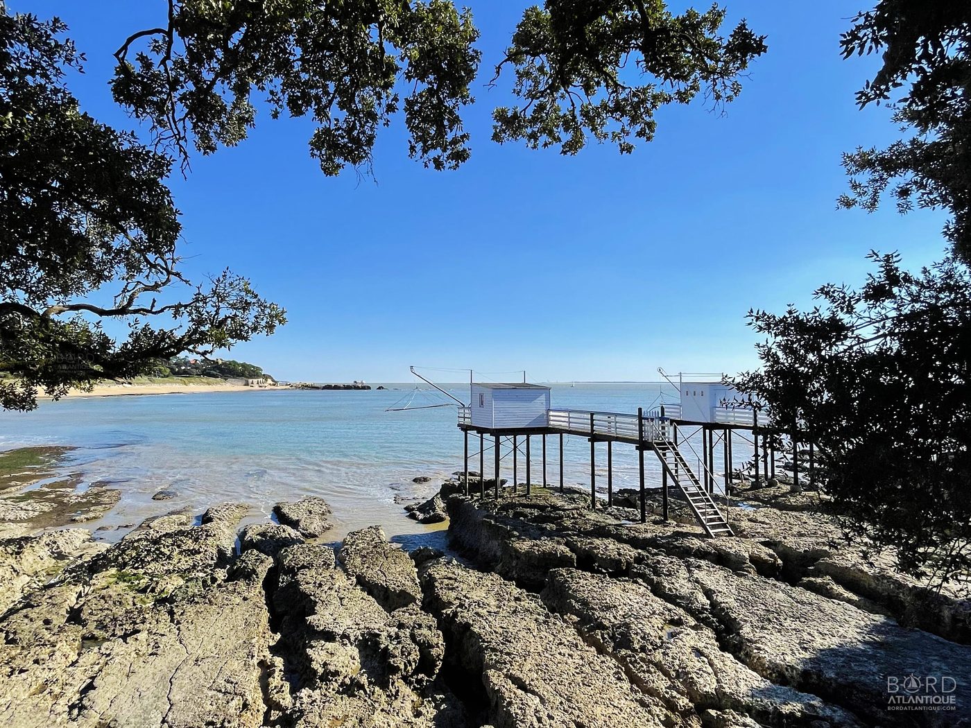 Deux carrelets blancs sur pilotis à la plage du Platin, Saint-Palais-sur-Mer, encadrés par les chênes verts